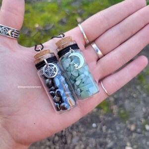 Peut inclure: Deux petites bouteilles en verre avec des bouchons en liège et une ficelle noire attachée autour du cou. Chaque bouteille contient de petites pierres et un charme. Une bouteille a un charme pentagramme et des pierres noires. L'autre bouteille a un charme de croissant de lune et des pierres vertes.