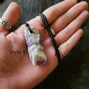 Peut inclure: Un collier pendentif en cristal naturel. Le cristal est un m&eacute;lange de teintes violettes, blanches et jaunes, suspendu &agrave; un cordon noir. Le texte "Style 1" est visible sur l'image.