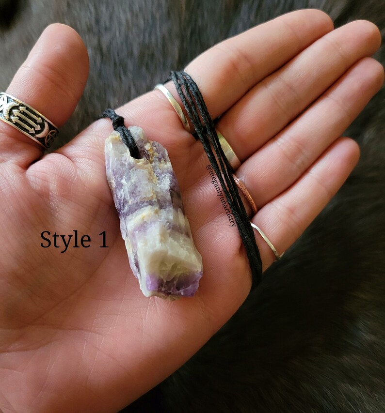 Peut inclure: Un collier pendentif en cristal naturel. Le cristal est un m&eacute;lange de teintes violettes, blanches et jaunes, suspendu &agrave; un cordon noir. Le texte "Style 1" est visible sur l'image.
