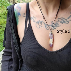 Peut inclure: Un collier avec un pendentif en cristal d'am&eacute;thyste rectangulaire et long. Le cristal est violet et blanc, suspendu &agrave; un cordon noir. Le texte "Style 3" est visible sur le c&ocirc;t&eacute; droit de l'image.