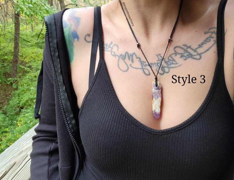 Peut inclure: Un collier avec un pendentif en cristal d'am&eacute;thyste rectangulaire et long. Le cristal est violet et blanc, suspendu &agrave; un cordon noir. Le texte "Style 3" est visible sur le c&ocirc;t&eacute; droit de l'image.