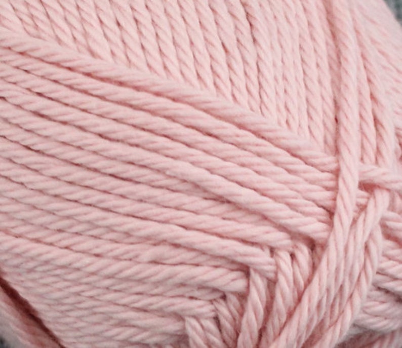 Op de afbeelding: Close-up van een zacht, roze garen. Het garen is gemaakt van katoen en is perfect om te breien of haken.