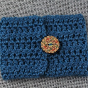 May include: A small blue crocheted pouch with a decorative wooden button. The button has a colorful floral design.