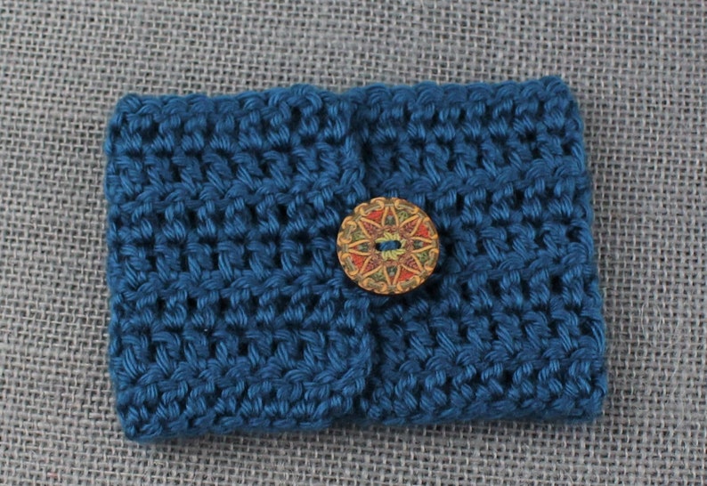 May include: A small blue crocheted pouch with a decorative wooden button. The button has a colorful floral design.