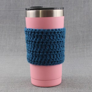 May include: A pink stainless steel tumbler with a blue crocheted cozy. The cozy is made with a simple stitch pattern and has a textured look.