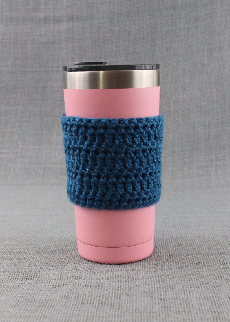 May include: A pink stainless steel tumbler with a blue crocheted cozy. The cozy is made with a simple stitch pattern and has a textured look.