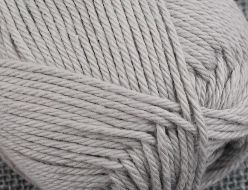 May include: A close-up of a skein of light gray yarn. The yarn is made of cotton and is soft and fluffy.
