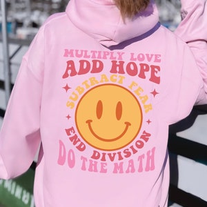 May include: Pink hoodie with a graphic design on the back that says "Multiply Love, Add Hope, Subtract Fear, End Division, Do The Math" with a smiley face in the center.