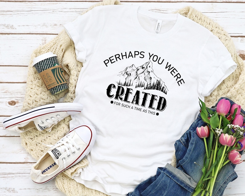 May include: White t-shirt with black text that reads "Perhaps you were created for such a time as this."  The text is surrounded by a graphic of mountains and trees.