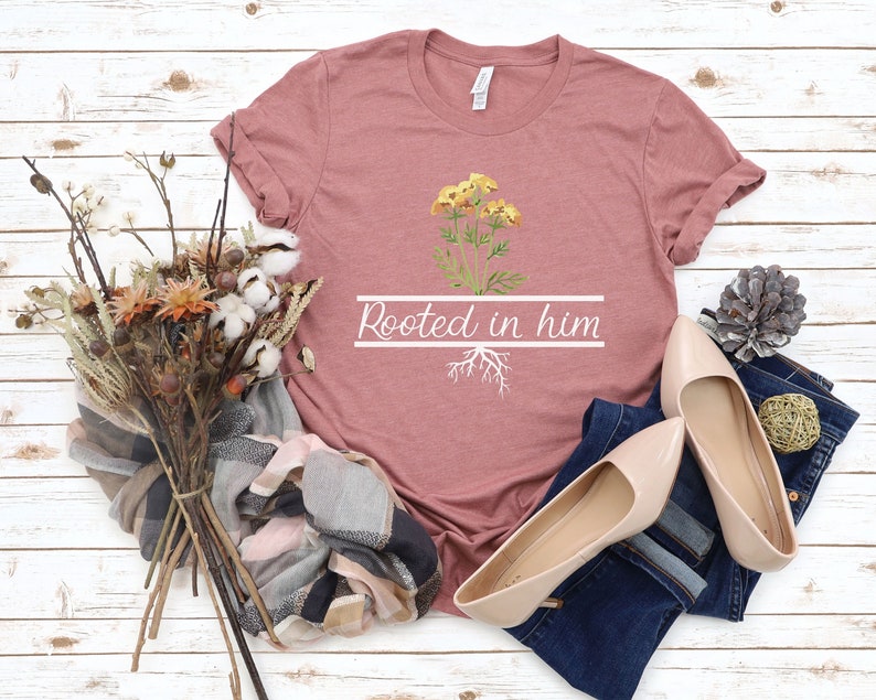 May include: A dusty rose t-shirt with a white graphic of a yellow flower with roots and the text "Rooted in him".