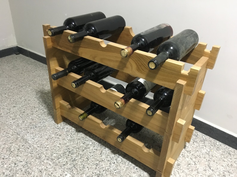 May include: A wooden wine rack with three shelves, holding multiple bottles of wine. The rack is made of light brown wood and has a simple, rustic design.