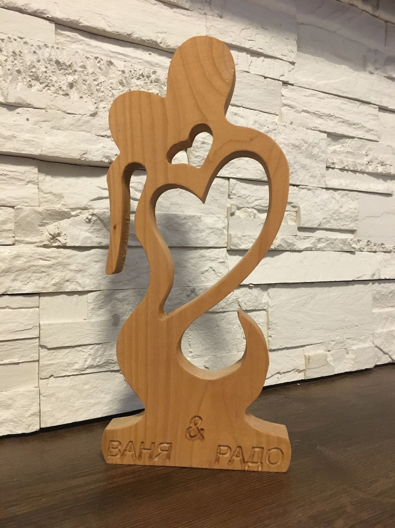 May include: Wooden sculpture of two figures embracing, carved with a heart shape. The base of the sculpture is engraved with the names "Ваня & Радо".