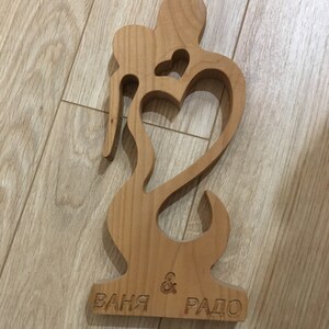 May include: A wooden cutout of two figures embracing, forming a heart shape. The base is engraved with the names "Ваня & Радо".