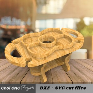 May include: Wooden serving tray with a guitar shape and multiple compartments. The tray has two handles and a lower shelf. The tray is made of light brown wood and is sitting on a wooden surface.