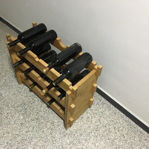 May include: A wooden wine rack with multiple bottles of red wine. The rack is made of light brown wood and has three shelves. The bottles are arranged in a staggered pattern.