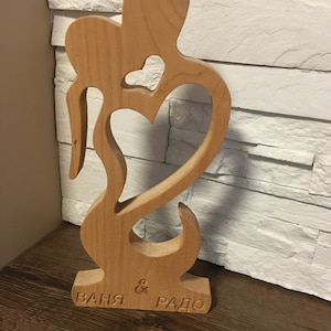May include: A wooden sculpture of two figures embracing, with a heart cutout in the center. The sculpture is inscribed with the names "Ваня & Радо".