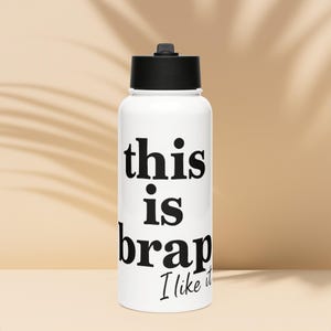 May include: White water bottle with a black lid and the text "this is brap I like it" in black. The bottle is cylindrical and has a black cap.
