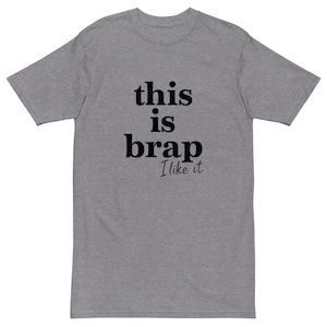 May include: A gray t-shirt with the text "this is brap I like it" in black. The shirt is a basic crew neck style, suitable for casual wear. The text is centered on the front of the shirt.