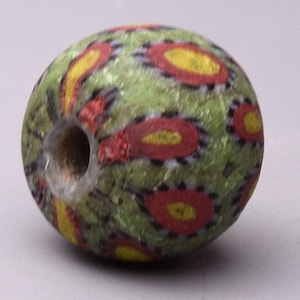 May include: A green glass bead with a hole in the center. The bead is decorated with red, yellow, and black swirls.
