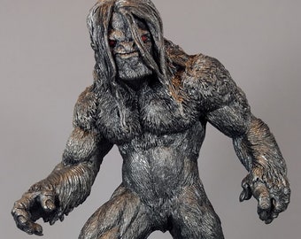 May include: A gray and black detailed figurine of a large, hairy creature with red eyes. The creature is standing on a rocky base.