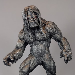 May include: A gray and black detailed figurine of a large, hairy creature with red eyes. The creature is standing on a rocky base.