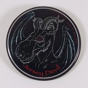 Puede incluir: Una ilustración en blanco y negro del Diablo de Jersey, una criatura mítica con alas, cuernos y una cabeza de caballo. La imagen está sobre un fondo redondo negro con un borde plateado. El texto "Jersey Devil" está escrito en rojo en la parte inferior de la imagen.