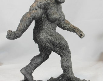 May include: A gray, sculpted figurine of Bigfoot, a mythical creature, walking on a rocky base. The figurine is detailed with fur and facial features.