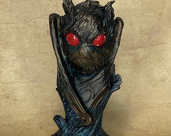 May include: A black and blue figurine of a creature with large red eyes and wings, standing on a tree stump.