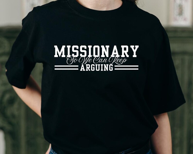 Puede incluir: Camiseta negra de cuello redondo con el texto blanco "MISSIONARY So We Can Keep Arguing". El texto est&aacute; en negrita, con una fuente decorativa para "So We Can Keep". Dos l&iacute;neas horizontales est&aacute;n debajo de la palabra "ARGUING". Una prenda casual.