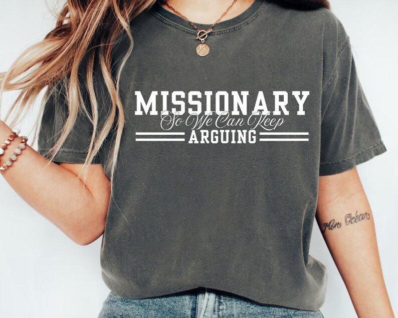 Puede incluir: Camiseta gris oscuro con el texto blanco "MISSIONARY So We Can Keep ARGUING". La camiseta tiene cuello redondo y mangas cortas. La tela parece suave y c&oacute;moda. Una prenda informal para todos los d&iacute;as.