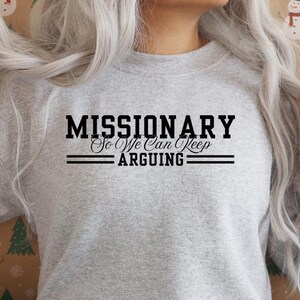 Puede incluir: Una sudadera gris claro con el texto negro "MISSIONARY So We Can Keep ARGUING". El texto est&aacute; centrado, con dos l&iacute;neas horizontales encima y debajo de "ARGUING". Es una prenda informal.