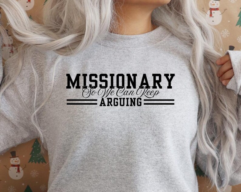 Puede incluir: Una sudadera gris claro con el texto negro "MISSIONARY So We Can Keep ARGUING". El texto est&aacute; centrado, con dos l&iacute;neas horizontales encima y debajo de "ARGUING". Es una prenda informal.