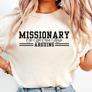 Puede incluir: Camiseta color crema con el texto negro "MISSIONARY So We Can Keep ARGUING". El texto est&aacute; en negrita y subrayado con dos l&iacute;neas horizontales. La camiseta tiene mangas cortas y cuello redondo.