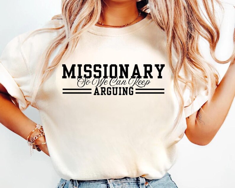 Puede incluir: Camiseta color crema con el texto negro "MISSIONARY So We Can Keep ARGUING". El texto est&aacute; en negrita y subrayado con dos l&iacute;neas horizontales. La camiseta tiene mangas cortas y cuello redondo.