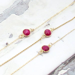 Peut inclure: Trois chaînes en or avec des accents de pierres précieuses rouges. Les chaînes sont superposées sur un fond blanc.