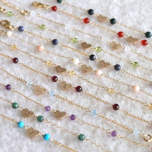May include: Gold chain bracelets with colourful gemstone beads and heart-shaped charms. Each charm features a zodiac symbol. The bracelets are displayed on a white surface, showcasing the variety of colours and designs.
