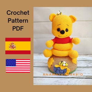 Puede incluir: Patrón de crochet PDF para un amigurumi de Winnie the Pooh. La muñeca es amarilla con una camisa roja y está sentada sobre una base de crochet marrón con abejas. El patrón está disponible en inglés y español.