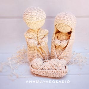 Puede incluir: Un belén tejido a ganchillo en color beige. El conjunto incluye tres figuras: dos adultos y un bebé en una cuna. El texto "ANAMAYAROSARIO" es visible en la parte inferior de la imagen.