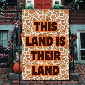 Puede incluir: Una bandera de jardín con el texto "THIS LAND IS THEIR LAND" en letras de bloque naranja. La bandera tiene un fondo crema con un patrón repetido de ilustraciones con temática otoñal en naranja y marrón.
