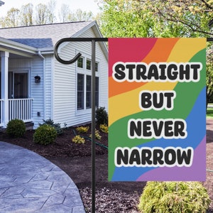 May include: A rainbow-coloured garden flag with the text "Straight But Never Narrow" in black lettering.