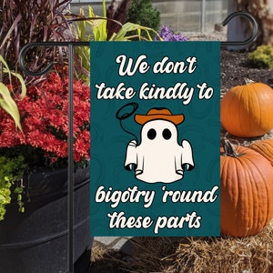 Può includere: Una bandiera da giardino di Halloween verde acqua con un fantasma bianco che indossa un cappello da cowboy e il testo "We don't take kindly to bigotry 'round these parts".
