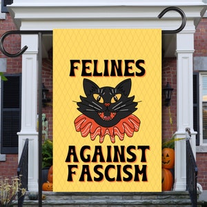 Può includere: Una bandiera da giardino gialla con le parole "FELINES AGAINST FASCISM" in lettere nere. La bandiera presenta un gatto nero dei cartoni animati con occhi arancioni e un colletto a balze. Lo sfondo ha un motivo a rombi.