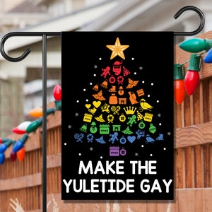 May include: A black garden flag with a Christmas tree design made of colorful holiday icons. The tree is topped with a gold star. The text "MAKE THE YULETIDE GAY" is printed in white at the bottom of the flag.