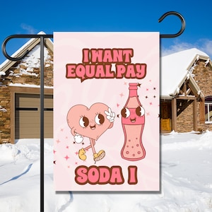 May include: A pink garden flag with a cartoon heart and soda bottle. The text on the flag reads "I want equal pay soda I".