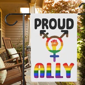 May include: A white garden flag with the text "PROUD ALLY" in rainbow colors. The flag also features a black and brown gender symbol with a raised fist in the center.