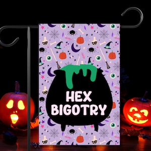 Può includere: Bandiera da giardino di Halloween viola con un calderone nero e liquido verde. Il calderone ha il testo "Hex Bigotry" su di esso. La bandiera è decorata con stelle, lune, ragni, pipistrelli e altre immagini di Halloween.