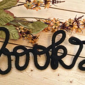 May include: Black yarn word art spelling out "books" on a light wood background.
