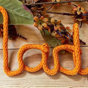 May include: The word "Made" spelled out in orange yarn, with a rustic wooden background.