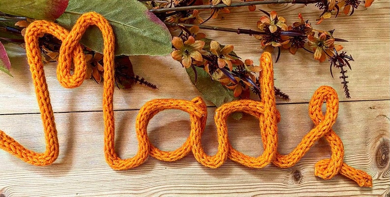 May include: The word "Made" spelled out in orange yarn, with a rustic wooden background.