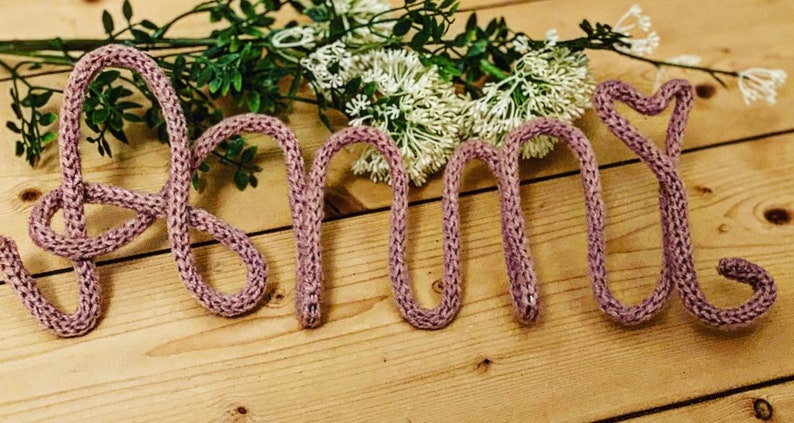 May include: The word "Amy" spelled out in pink knitted yarn.